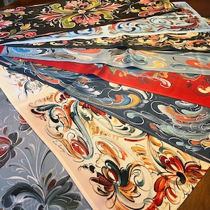 May include: A collection of rectangular fabric runners arranged in a fan shape, each featuring hand-painted floral and scrollwork designs in various colors including black, red, light blue, and cream, with the signature Ewa Zarychta visible.