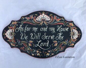 May include: A black wooden sign with a red border and white, red, and green floral designs. The sign reads "As for me and my house we will serve the Lord." The artist's signature, "Lise Lorentzen", is in the bottom right corner.