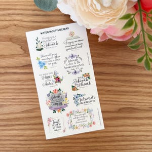 May include: A sheet of waterproof stickers with floral designs and inspirational quotes. The stickers feature phrases like "Throw your burden on Jehovah" and "We have this hope as an anchor." The stickers are on a wooden surface.