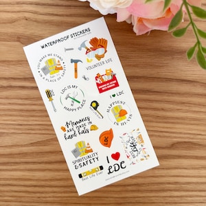 May include: A sheet of waterproof stickers with various construction-themed designs. The stickers feature tools, safety gear, and phrases like "Volunteer Life" and "Happy Place." The color palette includes orange, yellow, and blue, with the text "Waterproof Stickers" at the top.