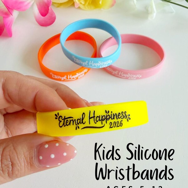 May include: A hand holds a yellow silicone wristband with the text "Eternal Happiness 2026". Other wristbands are orange, blue, and pink. The text "Kids Silicone Wristbands AGES 5-12" is also visible.