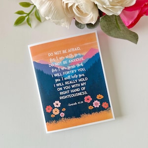 Puede incluir: Una tarjeta de cita inspiradora con un paisaje de montaña colorido y flores. La cita dice "No temas, porque yo estoy contigo. No te angusties, porque yo soy tu Dios. Te fortaleceré, sí. Te ayudaré. Te sostendré realmente con mi mano derecha de justicia." -Isaías 41:10