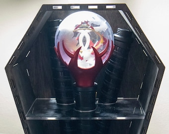 May include: A black wooden coffin-shaped display case with three black lightsaber-like objects and a red and white orb with a clear glass sphere on top.