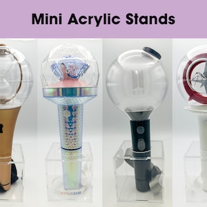 Puede incluir: Cuatro soportes de acrílico transparente que muestran diferentes palos de luz de colores. Los palos de luz son esféricos con un mango y llevan los nombres de grupos de K-pop: BTS, Seventeen y Stray Kids.