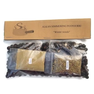May include: A brown cardboard box with the text "Alkan Simmering Potpourri" and "Winter Woods" on it. The box contains three small bags of potpourri ingredients: juniper berries, thyme, and rosemary.