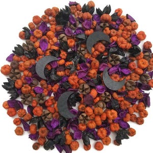 Puede incluir: Un arreglo temático de Halloween con mini calabazas naranjas, hojas moradas y detalles en negro. Tres medias lunas grises oscuras se intercalan en la decoración, creando un aspecto festivo de otoño.