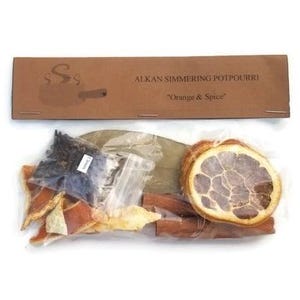 May include: A clear plastic bag filled with simmering potpourri ingredients, including orange peels, cinnamon sticks, cloves, and bay leaves. The bag is labeled "Alkan Simmering Potpourri "Orange & Spice""