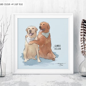 Framed illustration of two dogs, one golden and one yellow, wearing bandanas, with names "Gumbo" and "Aslan" labeled. The frame sits on a white table with minimalistic decor and a light blue background.