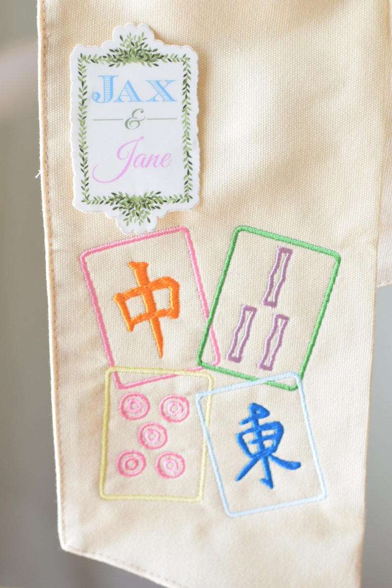 May include: Cream-colored fabric with embroidered Mahjong tiles in various colors. The tiles feature Chinese characters and symbols. A decorative label at the top reads "Jax & Jane" in blue and pink.