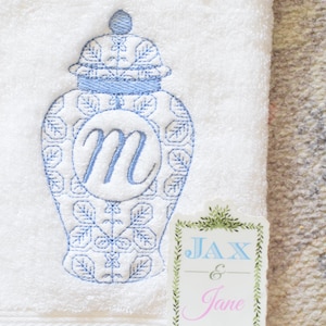 May include: White towel with a blue embroidered ginger jar design and the letter "m". A sticker with the names "Jax & Jane" is also visible. The towel is made of a soft, absorbent material.
