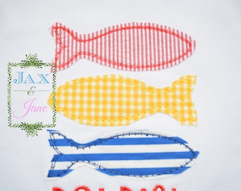 May include: Three felt fish appliques in red and white stripes, yellow gingham, and blue and white stripes. The fish are arranged vertically with the red and white fish at the top and the blue and white fish at the bottom.
