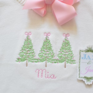 Op de afbeelding: Witte gebreide trui met geborduurde kerstboompjes en de naam "Mia" met een snoepstokontwerp. Een apart geborduurd patchje staat "Jax & Jane".