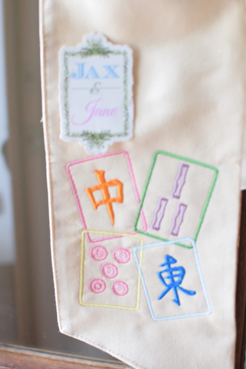 May include: Cream-colored fabric with embroidered Mahjong tiles and a decorative label that reads "Jax & Jane". The tiles feature colorful symbols and characters, perfect for game enthusiasts.