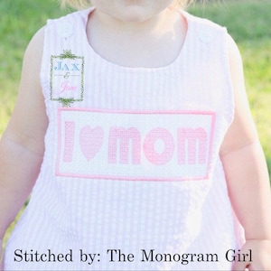 May include: A pink and white striped onesie with a pink embroidered heart and the words "I love mom" on the front. The onesie has a small label with the text "Jax & Jane" on the front.