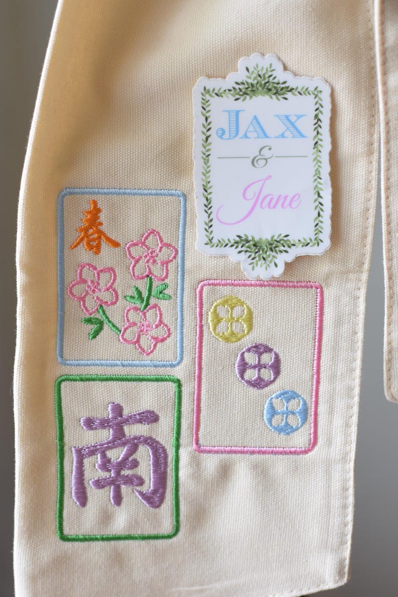 May include: Cream-colored fabric with embroidered designs. Features a sticker with the names "JAX & Jane" and floral accents. The embroidered squares include floral and Chinese character motifs in various colors.