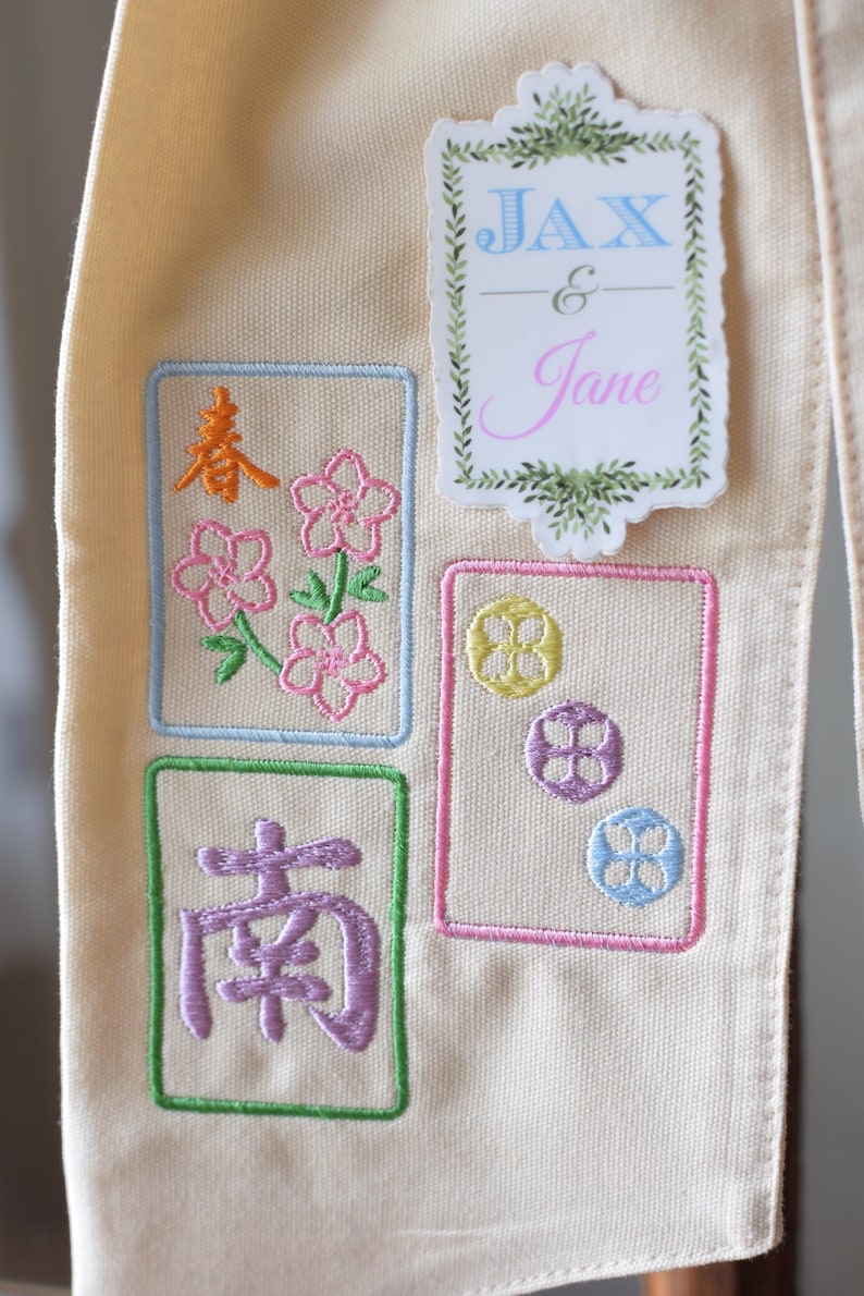 May include: Cream-colored fabric with embroidered designs. Features floral and Chinese character motifs in pink, orange, green, and purple. Includes a sticker with the names "JAX & Jane" in blue and pink.