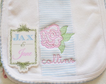 May include: White bib with blue and white stripes, a pink embroidered rose, and a green embroidered label with the text "Jax & Jane Collins".