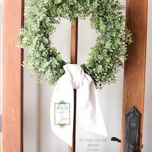 May include: A green wreath with a white ribbon and a sign that says "JAX & Jane" hanging on a wooden door.