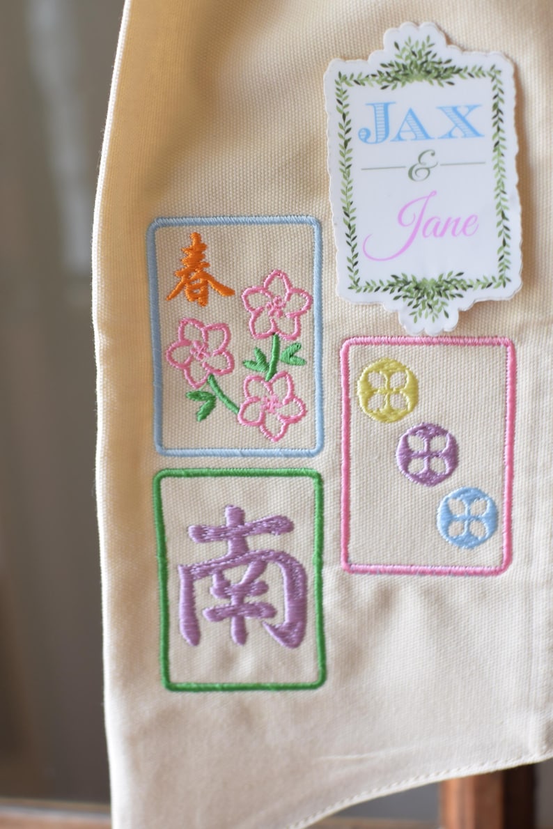 May include: Cream-colored fabric with embroidered designs. Features floral and geometric patterns in pink, orange, green, and blue. Includes the text "JAX & Jane" in a decorative frame.