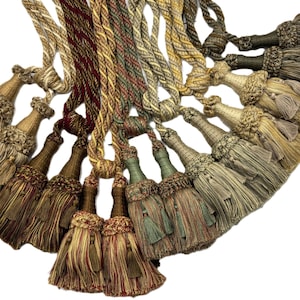 May include: A selection of decorative tassels in shades of gold, brown, green, and red. The tassels feature a braided rope design, suitable for home decor or craft applications.