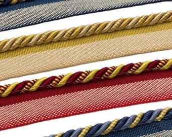 Könnte beinhalten: Vier Streifen dekorative Borte mit gedrehter Kordelkante. Die erste ist marineblau und gold, die zweite beige und gold, die dritte rot und gold und die vierte hellblau und gold. Jede Borte hat eine flache Basis aus gewebtem Stoff.
