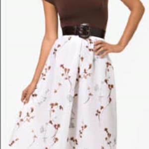 May include: A brown cap-sleeve top paired with a white midi skirt featuring a floral pattern. A black belt cinches the waist. The outfit is completed with silver high-heeled sandals.