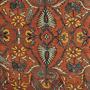 May include: Detailed shot of a patterned fabric with a repeating floral design. The pattern includes stylized yellow and grey flowers, white and grey leaf-like shapes, and bird motifs, set against a reddish-brown backdrop. The design is symmetrical.