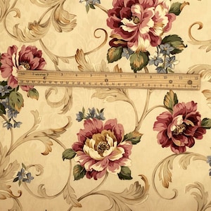 K&ouml;nnte beinhalten: Florale Tapete mit gro&szlig;en burgunderfarbenen und cremefarbenen Pfingstrosenbl&uuml;ten, gr&uuml;nen Bl&auml;ttern und blauen Akzenten. Das Design umfasst beige Ranken auf cremefarbenem Hintergrund. Ein Lineal zeigt den Ma&szlig;stab des Musters.