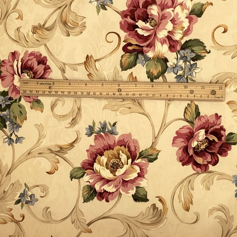 K&ouml;nnte beinhalten: Florale Tapete mit gro&szlig;en burgunderfarbenen und cremefarbenen Pfingstrosenbl&uuml;ten, gr&uuml;nen Bl&auml;ttern und blauen Akzenten. Das Design umfasst beige Ranken auf cremefarbenem Hintergrund. Ein Lineal zeigt den Ma&szlig;stab des Musters.