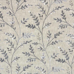 May include: A fabric featuring a light beige background with a textured, woven appearance. The surface is decorated with a repeating pattern of dark gray and silver-toned leafy branches that extend vertically across the entire material.