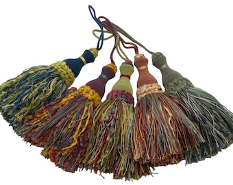 May include: A collection of five decorative tassels featuring wrapped cord tops and multi-textured, multi-coloured fringe skirts. The tassels display a palette of navy blue, deep plum, olive green, terracotta, and sage green, each with a hanging loop.