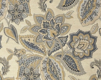 May include: A close-up of a beige fabric with a repeating floral pattern. The design features large stylized flowers and leaves in shades of blue, gray, and gold. The fabric has a textured appearance, suggesting a woven material.
