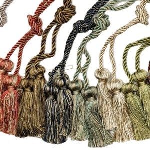May include: Assortment of 10 pairs of tassel tiebacks in various colors, including beige, red, gold, green, and blue. Each tieback features a twisted rope design and two tassels.