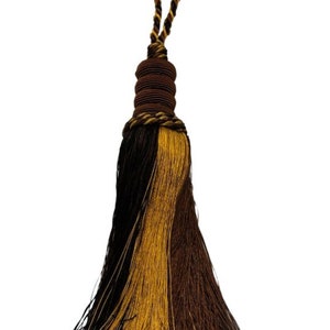 May include: A brown and gold tassel with a braided cord. The tassel is made of two different colors of yarn, brown and gold, and is tied together at the top with a brown cord.