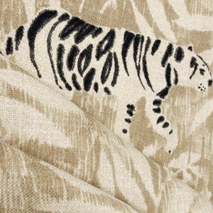 May include: Close-up of a beige fabric with a tiger design. The tiger is depicted in black and off-white, with a textured appearance. The fabric has a woven texture and a neutral color palette.