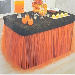 May include: A decorated banquet table with a black sequined top and an orange tulle skirt. The table is set with drinks, cupcakes, and candy. The Simplicity logo is in the top right corner. The image is for a party.