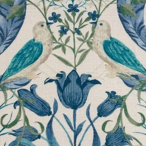 Op de afbeelding: Stofpatroon met twee vogels met turquoise vleugels en beige lichamen, omringd door blauwe bloemen en groene bladeren. Het ontwerp omvat gestileerde blauwe tulpen en kleine blauwe bloesems op een crèmekleurige achtergrond.
