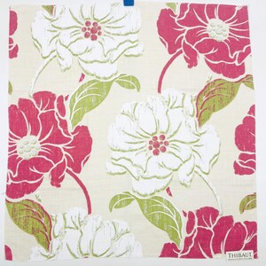 May include: A square fabric swatch featuring a floral pattern with large white and magenta flowers on a light beige background. The design includes green leaves and stems with a textured print effect. A small white label reads THIBAUT.