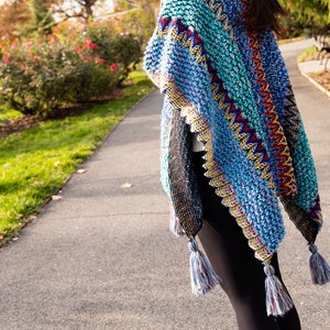 Puede incluir: Un chal de ganchillo colorido con un patr&oacute;n geom&eacute;trico y flecos. El chal est&aacute; hecho con una variedad de colores, incluyendo azul, verde, amarillo, rojo y negro.