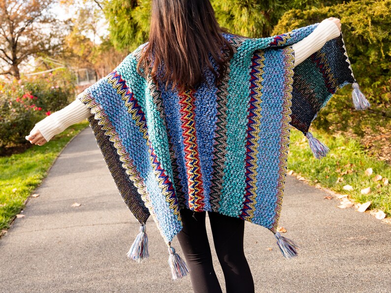 Puede incluir: Un poncho de crochet a rayas de colores con flecos. El poncho es azul, verde, rojo, amarillo y negro.