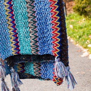 Puede incluir: Una manta de crochet colorida con flecos. La manta est&aacute; hecha de una variedad de colores, incluyendo azul, verde, rojo y amarillo.