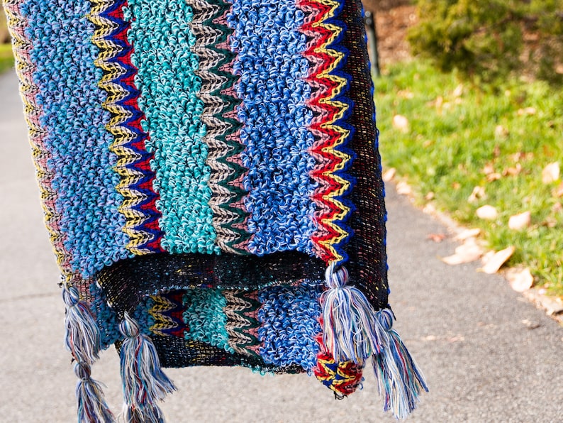 Puede incluir: Una manta de crochet colorida con flecos. La manta est&aacute; hecha de una variedad de colores, incluyendo azul, verde, rojo y amarillo.
