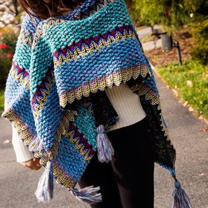Puede incluir: Un poncho de punto colorido con flecos. El poncho est&aacute; hecho de un hilo suave y texturizado y presenta una variedad de colores, incluyendo azul, verde, rojo y amarillo.