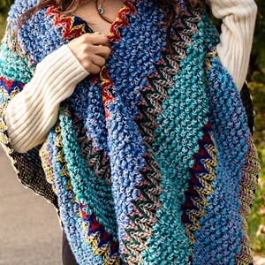 Puede incluir: Un poncho de crochet colorido con un dise&ntilde;o texturizado y abultado. El poncho est&aacute; hecho con una variedad de colores, incluyendo azul, verde, rojo y amarillo.