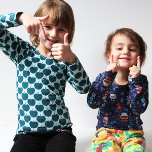 May include: Two children, one wearing a teal long-sleeved shirt with a green apple print and the other wearing a blue long-sleeved shirt with a robot print, are smiling and making a frame with their hands.
