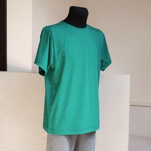 Può includere: Una maglietta verde a maniche corte su un manichino. La maglietta ha una texture melange.