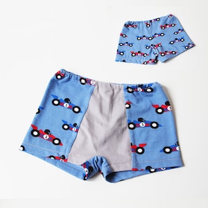 Op de afbeelding: Twee paar blauwe en grijze boxershorts met een rode en blauwe raceautoprint. Het grotere paar heeft een grijs paneel op de rug.