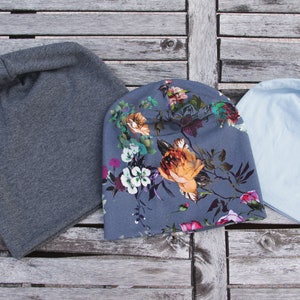 Puede incluir: Tres gorros de punto en diferentes colores y patrones. Uno es gris, otro es azul claro y otro tiene un patrón floral.