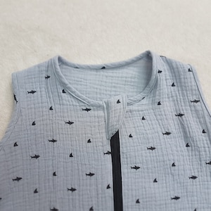 Puede incluir: Un saco de dormir para beb&eacute; sin mangas de color azul claro con un patr&oacute;n de tibur&oacute;n y aleta negros.
