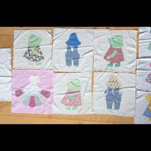 May include: A collection of 10 handmade fabric squares featuring appliqued figures of children wearing hats and dresses. The squares are made of white fabric with a pink square in the center featuring a white appliqued dress.
